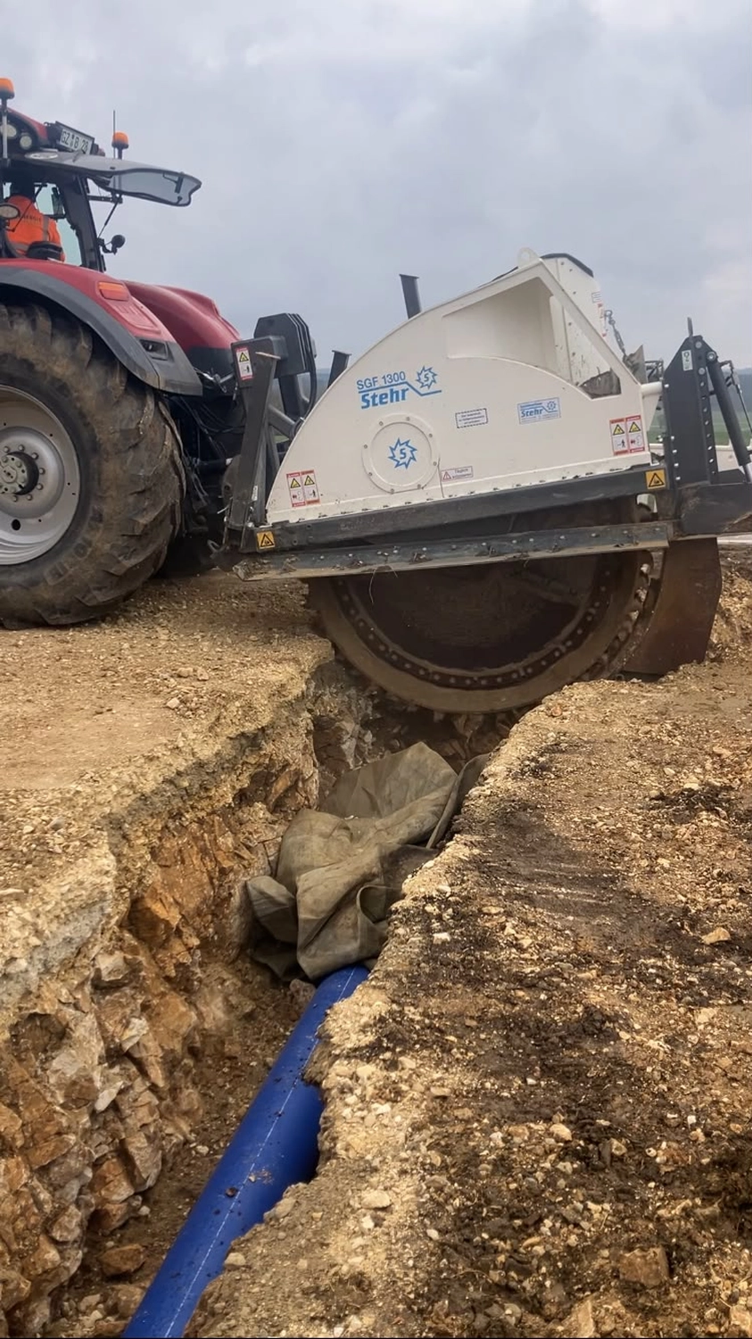 Bioenergie Fischerhöfe - Erschließung in Bodenklasse- Ein roter Traktor ist auf einer Baustelle im Einsatz Bodenklasse 6.